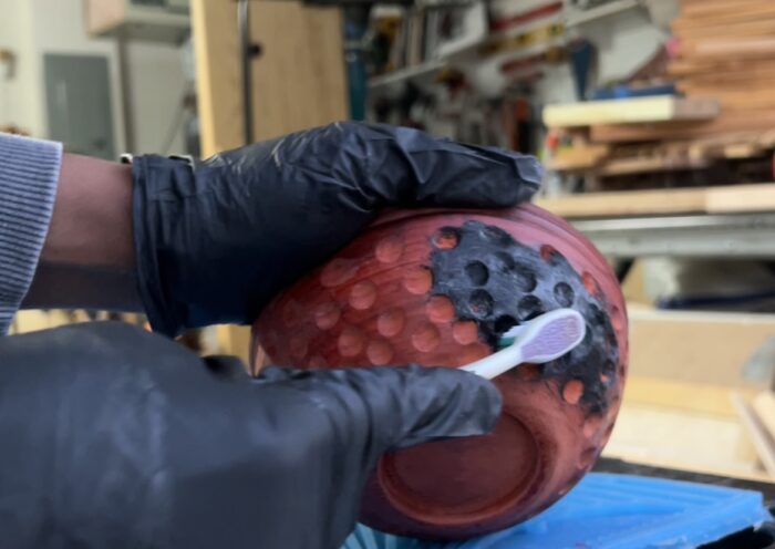 Char brushes a black dye onto the padauk bowl to highlight the carved divots. 