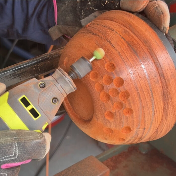 Char uses a rotary tool to carve divots in a padauk bowl.