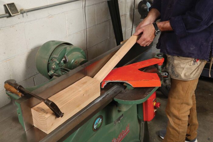 A stop block is attached the the end of a jointer and a chair leg is being placed against the stop block onto the jointer.