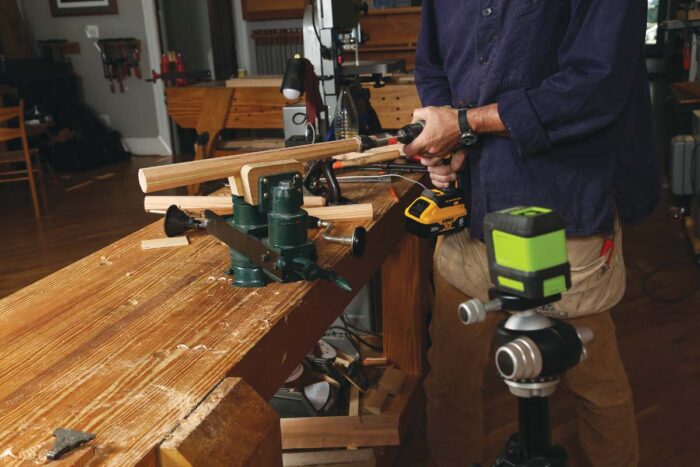 The chair leg is held in a vise and a plug cutter is being used to create a tenon on the end of it. 