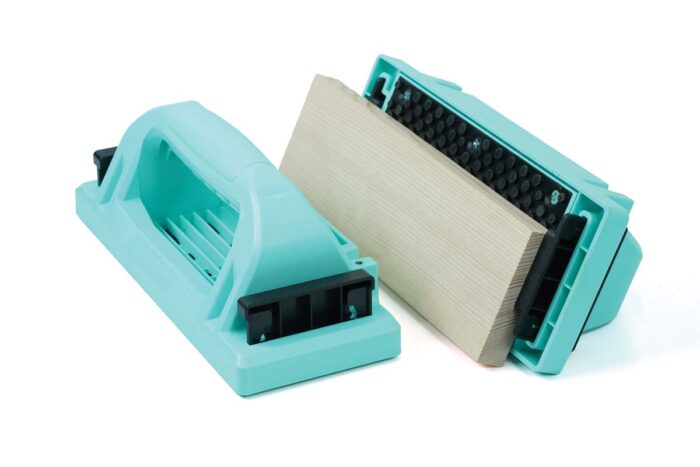 Two turquoise push blocks: one sitting upright and the other turned on its side so the bottom is visible. A black plastic tab at the back of the push block goes down to hook against whatever work piece you are using. 