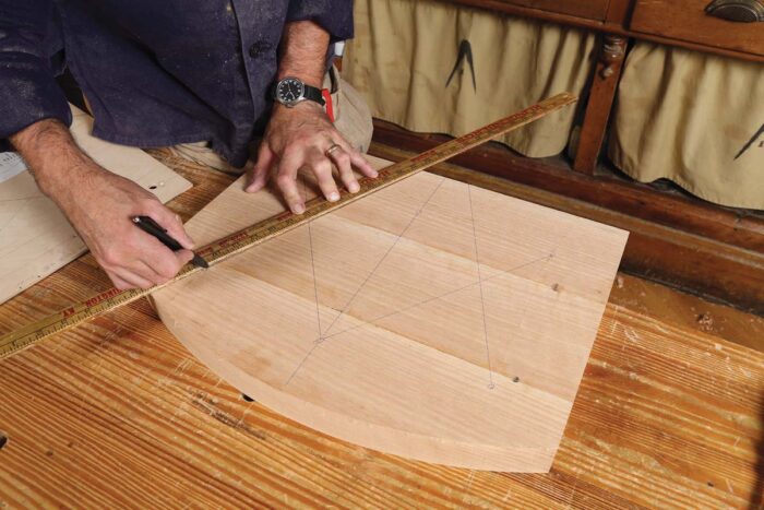 A chair seat is placed on the bench and Schwarz is using a ruler to draw lines between point.