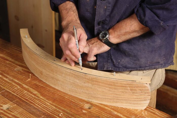 A template is placed on the curved board and holes are being transferred with a pencil.