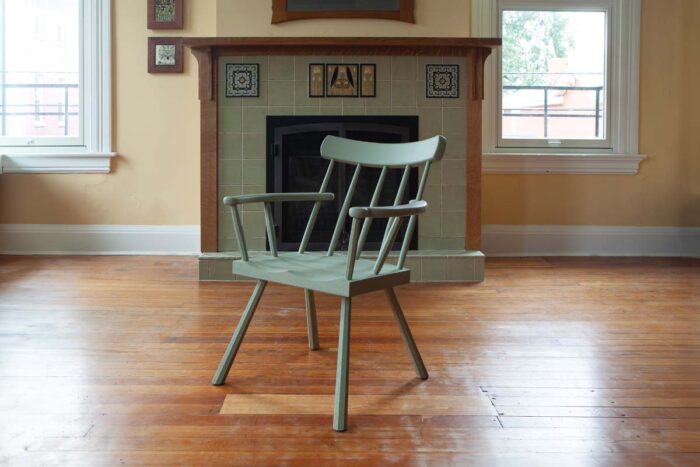 A painted chair sites in an empty room. The chair is painted a sage green. 