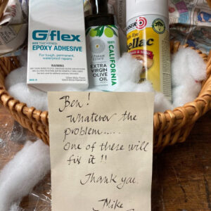 A gift basket with epoxy, olive oil, and shellac. A note is on top that reads: Ben! Whatever the problem... one of these will fix it!! Thank you, Mike"