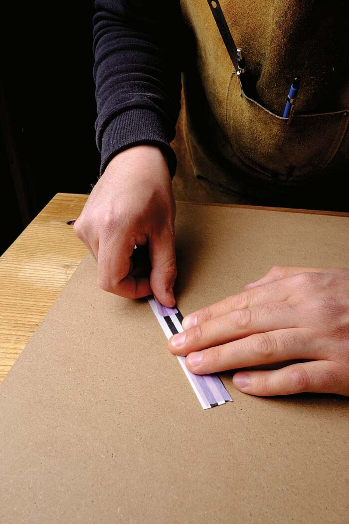 Vasko uses purple tape to secure strips of black and white veneer together. 