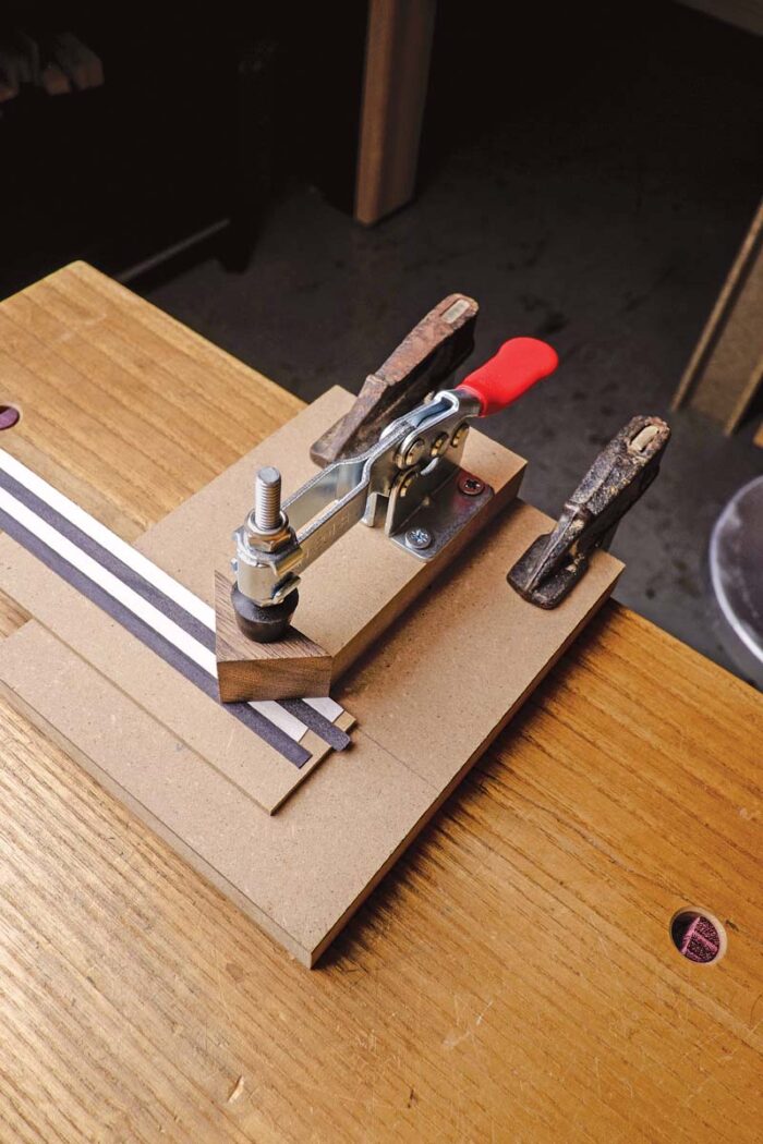 Vasko uses a shop made jig that utilizess a toggle clamp to hold down a triangle onto the veneer. This acts as a guide for his chisel.