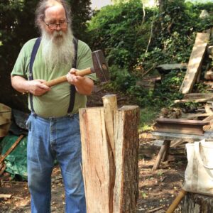 Peter standing splitting a piece off of a log