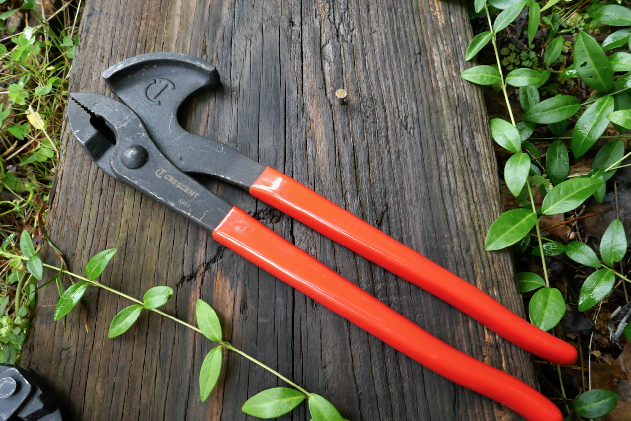 A nail extractor tool with pliers that have a curved surface on one side and red rubber handles.