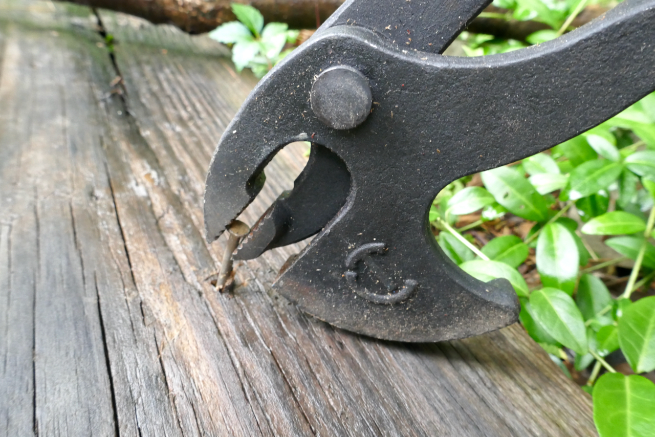 Pliers pulling a nail from a reclaimed board.